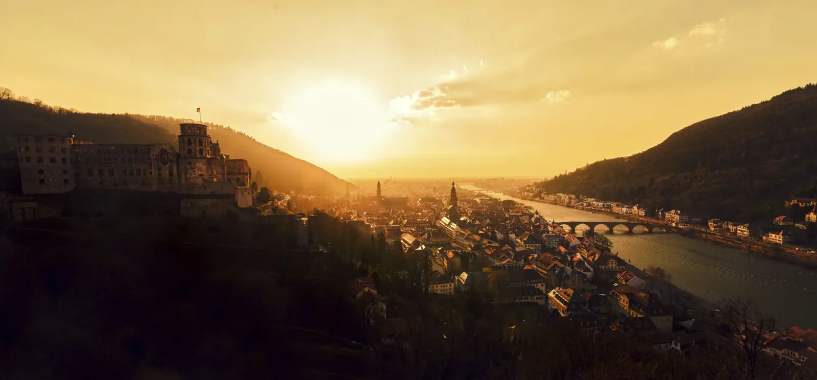 A castle above a river valley in the haze of the low sun