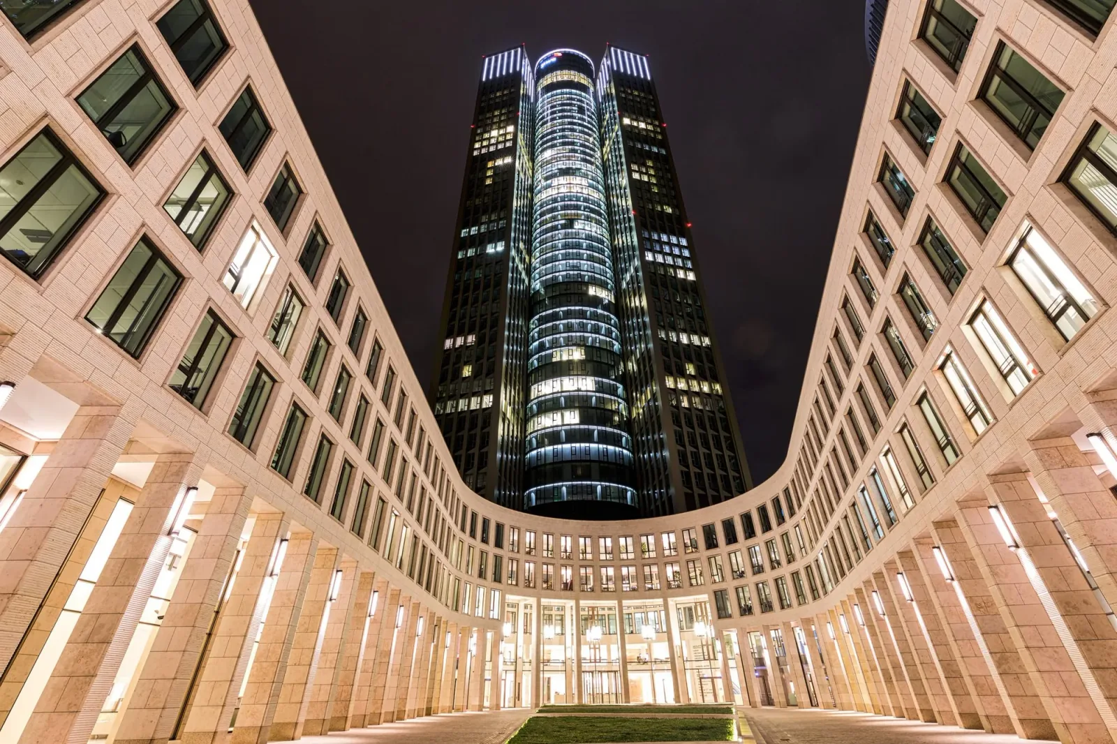 A lit high-rise at night, framed by two curved wings of a building