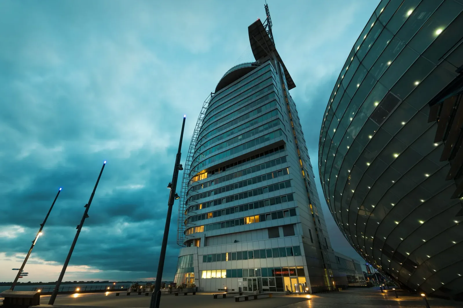 A curved tower and a domed glass facade under a teal evening sky