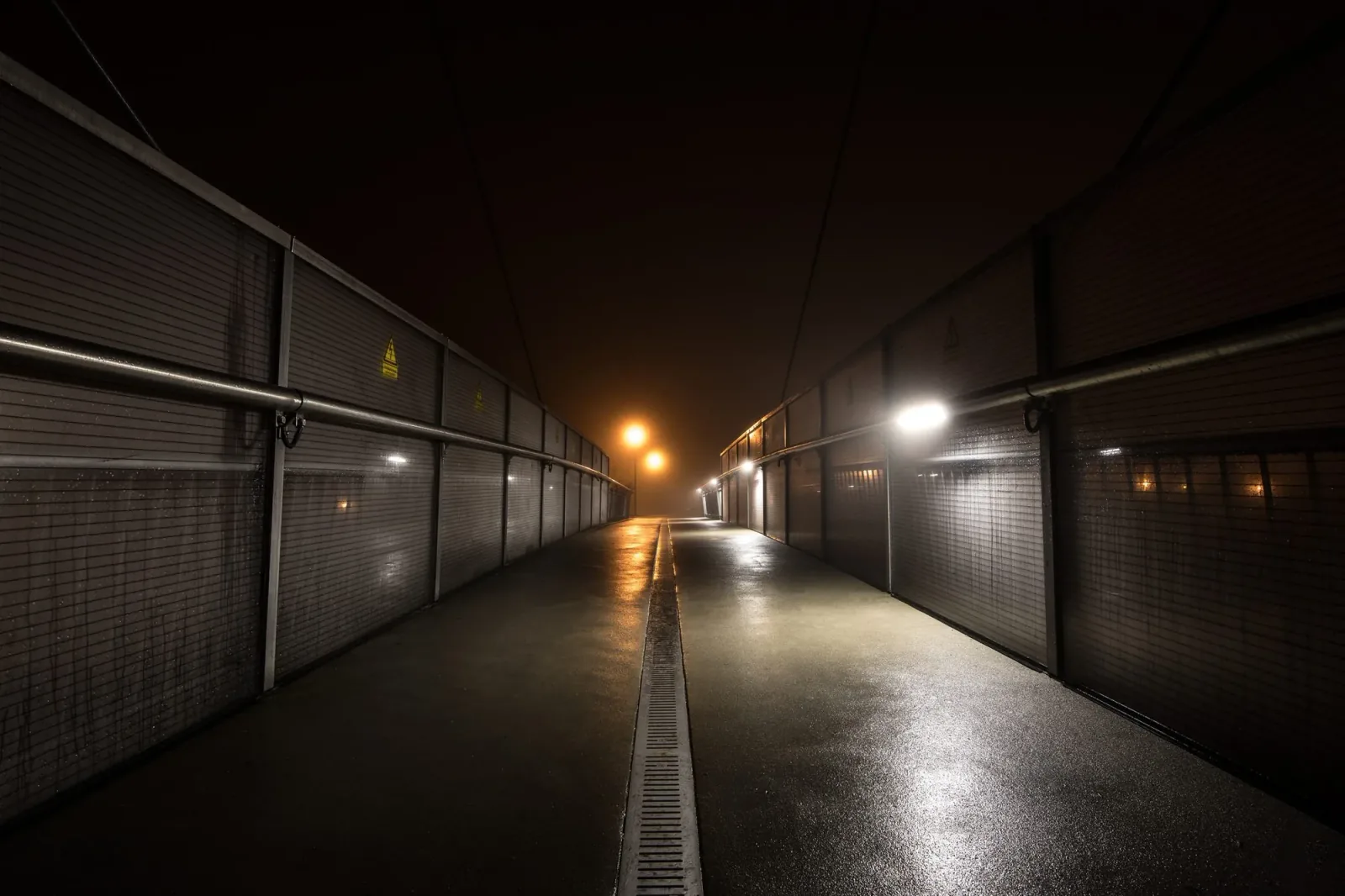 A wet, empty passage with a single lamp at its end
