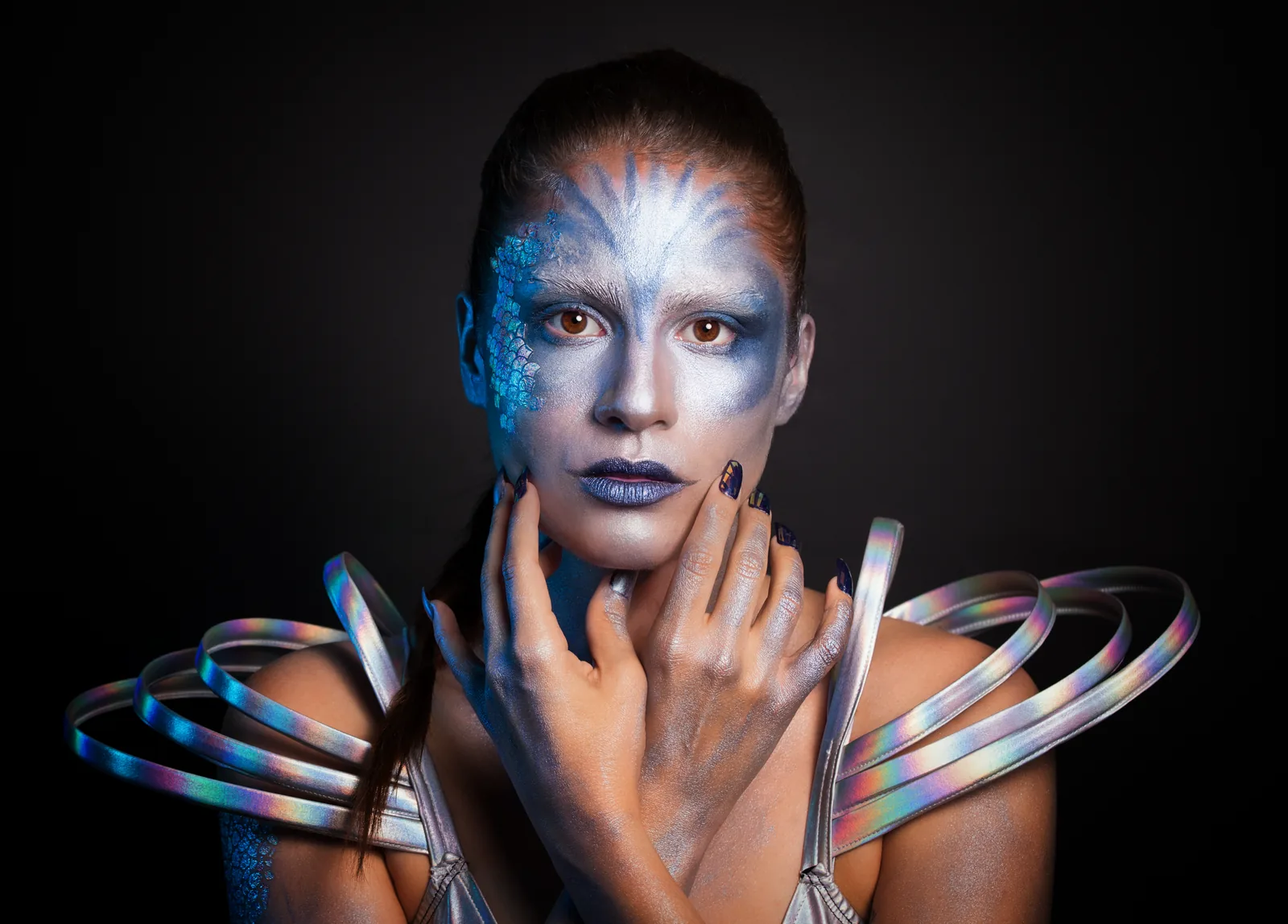 A face in silver body paint with iridescent rings around the shoulders