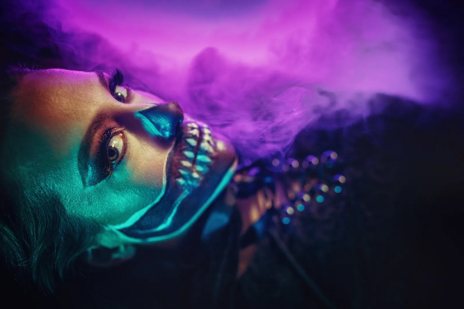 A face in turquoise and violet light, lying in haze