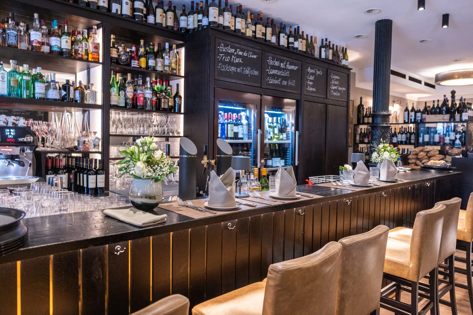 Lange Bar mit Barhockern und einer Wand aus Wein- und Spirituosenflaschen