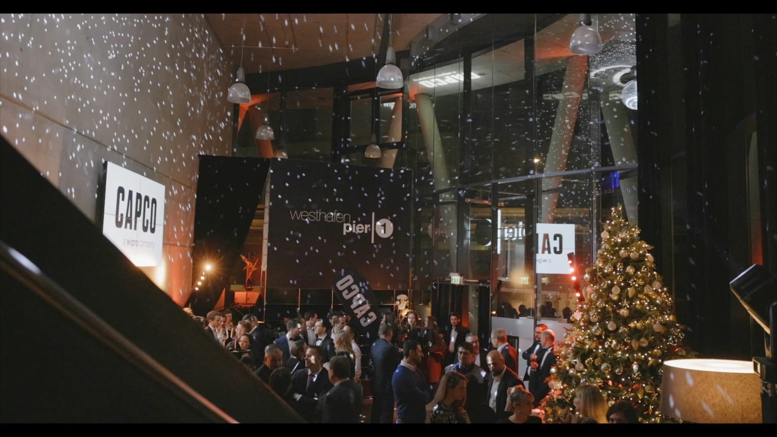 A frame from the Capco Christmas event with a decorated tree and projected snowflakes