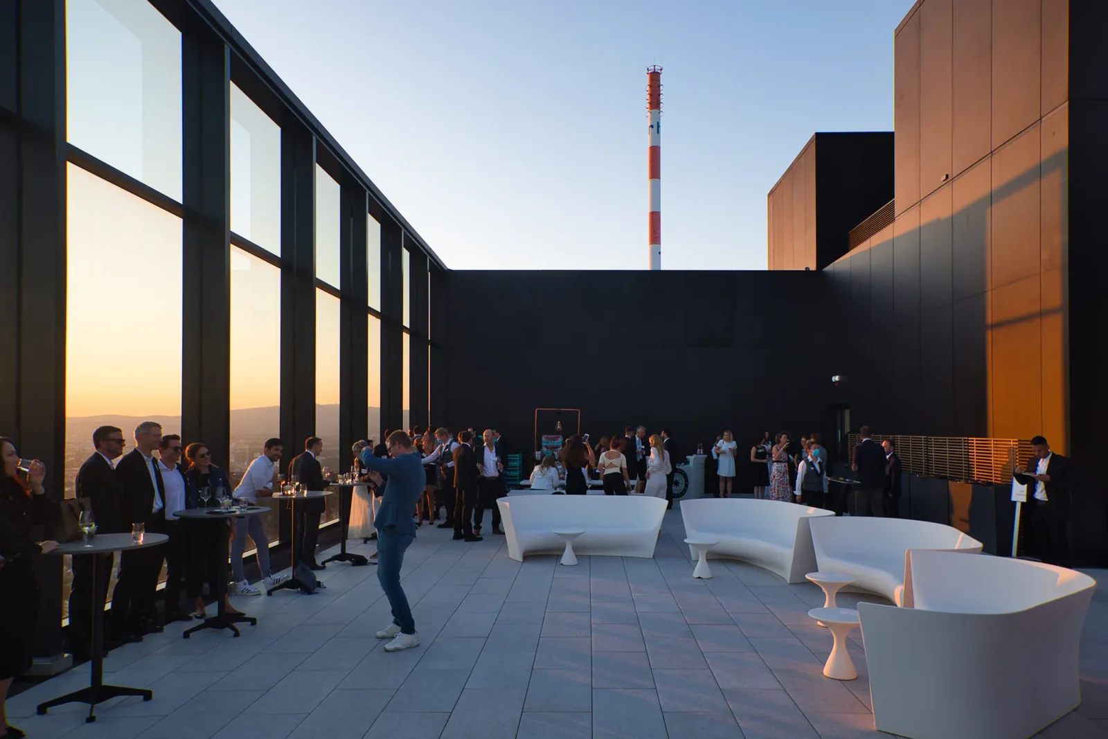 Dachterrasse mit Loungemöbeln und Gästen im Licht der untergehenden Sonne