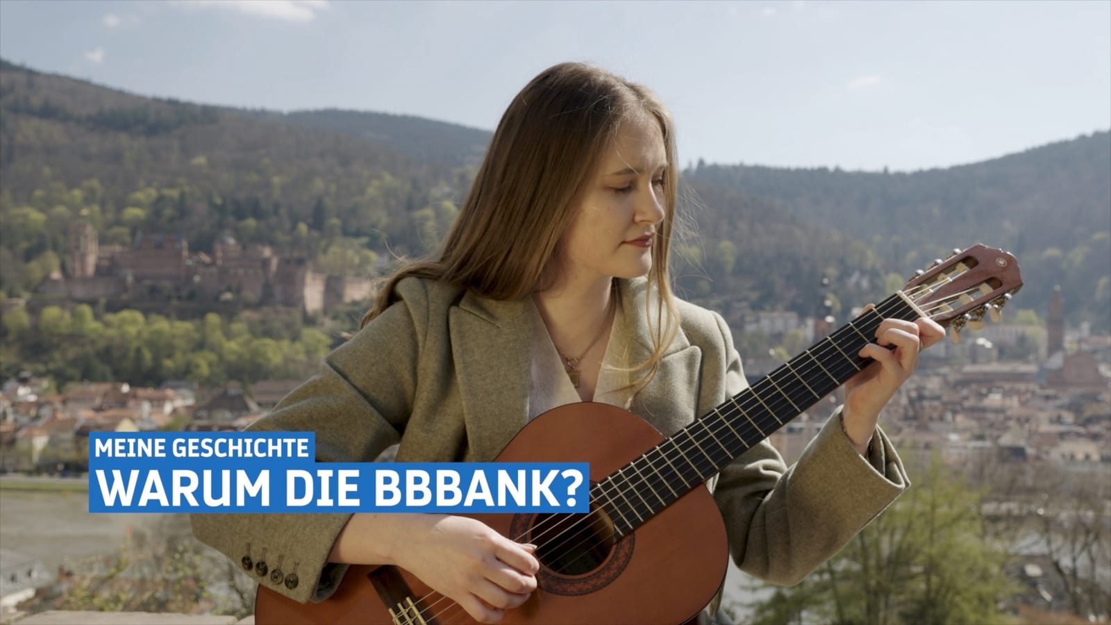 A frame from the BBBank trailer: a young woman playing guitar above the roofs of Heidelberg, with the caption “My story – why BBBank?” overlaid