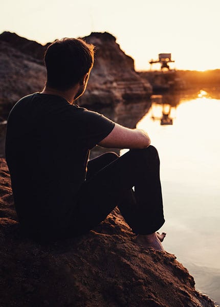Person am Ufer im Gegenlicht der tiefstehenden Sonne