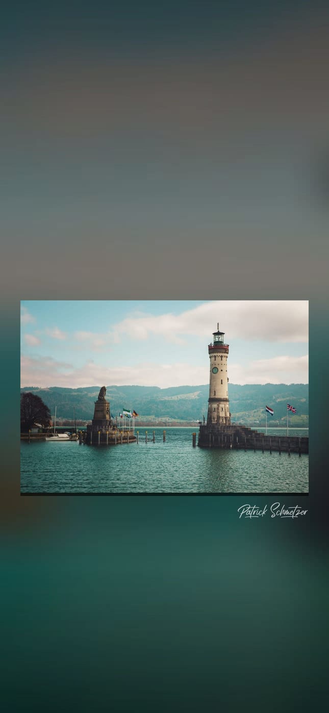 Hafeneinfahrt mit Löwenstatue und Leuchtturm vor den Bergen